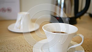 Close-up of person hand stirring coffee with spoon in a white cup on wooden table background.