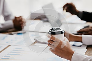 Close-up of person holding a paper coffee cup, business meeting, startup company sales team meeting, brainstorming and sales