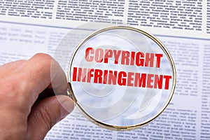 Person Holding Magnifying Glass Over Copyright Infringement Word photo