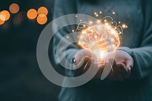 A close-up of a person\'s hands holding a glowing brain shaped light bulb, representing innovative ideas