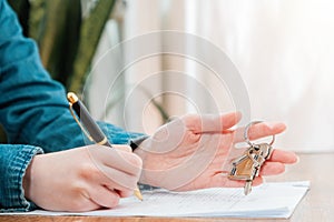 Close up of person signing a contract for the rental or purchase of real estate, holding the keys in his hands. Mortgage