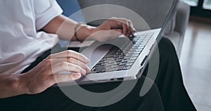 Close-up person sitting on couch at home and using laptop computer to work from home. Closeup male hands typing text on