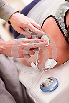 Close-up of a personal trainer hand putting an electrostimulator electrodes in the shoulder of a female deportist photo