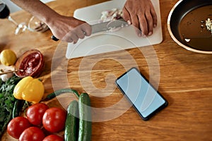 Close up of phone with blank screen on the table. Man cutting onion on chopping board, using smartphone app while