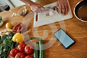 Close up of phone with blank screen on the table. Man cutting onion on chopping board, using smartphone app while