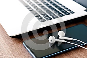 Close-up phone earbuds and laptop on wooden table