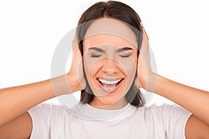 Close up photo of angry young woman plugging ears with hands and screaming