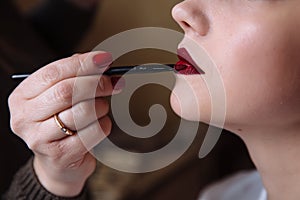 Close-up photo applying lipstick on the lips. Lip makeup with red pigment. Red matte lipstick on the lips of a young