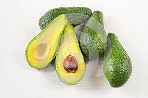 Close-up photo of avocados cut to half, brown seeds visible, with more avocados on white wooden background.