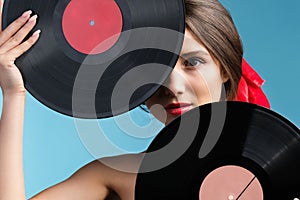 Close up photo of a beautiful girl likes music holding two vynil music records hiding partly her face over blue