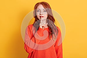 Close up photo beautiful lady with red pomade, long red hairstyle, keeping index finger near mouth, wearing casual orange sweater