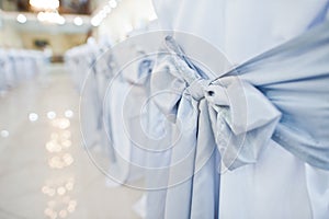 Close-up photo of big blue bows tied on white wedding chairs.