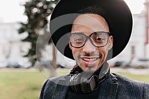 Close-up photo of blissful african male model with dark eyes standing on blur nature background. Outdoor portrait of