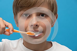 Close up photo blond boy with toothbrush and toothpaste brushing his teeth.