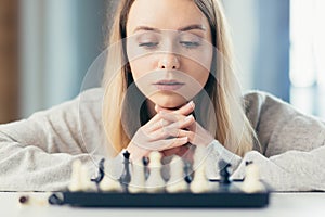 Close-up photo of a blonde woman playing chess, thoughtfully making a move