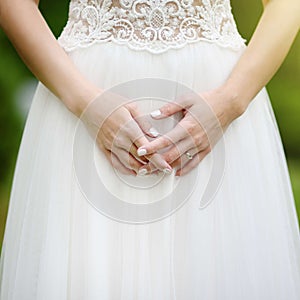 Close-up photo of bride`s hands with golden engagement ring on beautiful white wedding dress