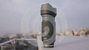Close up of photo camera lens standing on a building roof edge on blurred city background. Action. Presentation of a