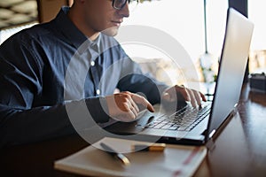 Close-up photo of caucasian male hands typing on laptop keyboard and using touchpad. Notebook and pen on foreground of