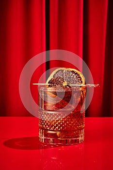 Close-up photo of cocktail with ice cubes, elegancy garnished orange slice served on red bar counter in restaurant