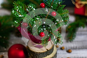 Close-up photo of coniferous branches, with Christmas toys and imitation of snow, standing in a vase on a wooden table.