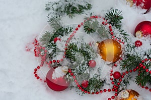 Close up photo of a coniferous branches decorated with toys for the Christmas tree lie in the snow on the right side of the frame