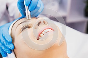 Close-up photo of cosmetologist doing hydrafacial microdermabrasion procedure in cosmetology clinic to a happy smiling