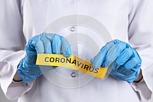 Close-up photo of doctor in gloves tearing coronavirus written paper