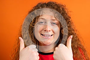 Close up photo of a fan football redhead woman in red clothes showing two thumbs up as a sign of good team game.