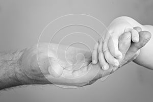 Close up photo of father holding baby hand in black and white