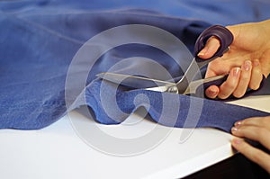 Close up photo of female hand with the scissors cutting the violet fabric