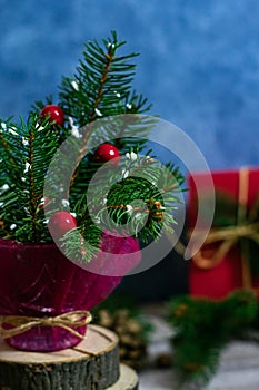 Close up photo of a fragment of coniferous branches in a vase on a wooden stand and red gift box in the background