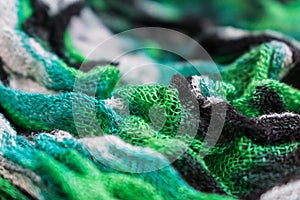 Close-up photo of the fragment of multicolored green, black and white colored fabric texture scarf.