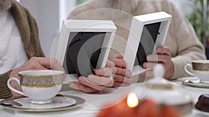 Close-up photo frames in male senior Caucasian friends hands. Unrecognizable old men sitting at table watching