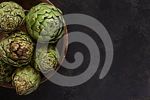Close up photo of fresh artichoke in the old wooden bowl. Top view on dark background