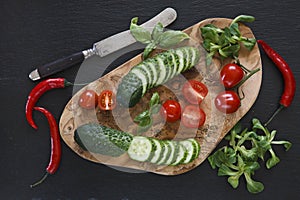 Close-up photo of fresh vegetables on wooden cutting board with knife on black concreted table background
