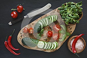 Close-up photo of fresh vegetables on wooden cutting board with knife on black concreted table background.