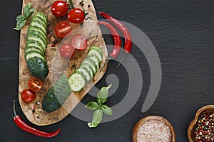 Close-up photo of fresh vegetables on wooden cutting board with knife on black concreted table background. Top view