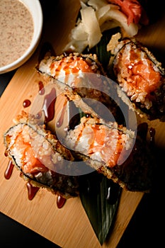 Close-up photo of fried salmon tempura sushi roll sandwich covered in sauce