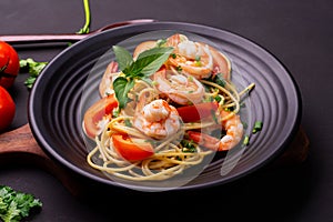 Close-up photo-fried spaghetti or fried noodles Pasta with tomato sauce and shrimp, basil, and tomatoes on a black plate On a