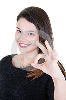 Close-up photo of funny young brunette woman in black sweater showing OK gesturein white background