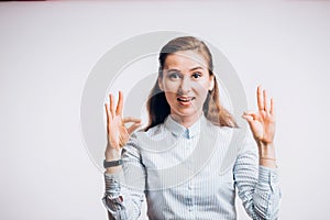 Close up photo of funny young brunette woman showing OK gesture, looking at camera on white background.