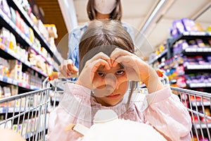 Close up photo of a girl making heart sign with her hands and having serious look, young woman pushing the cart wearing