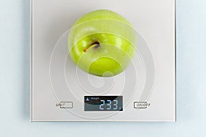 Close up photo of green fresh apple on gray digital kitchen scales. Blue background. Flat lay, top view.