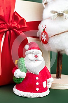 Close-up photo of gypsum colorful santa claus on the gift box and christmas tree with decorations over green background.