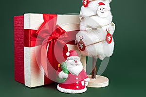 Close-up photo of gypsum colorful santa claus on the gift box and christmas tree with decorations over green background.