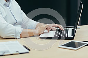 Close-up photo. Hands of a working young man behind a laptop, typing on a keyboard, in a office.