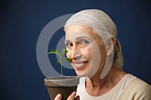 Close-up photo of happy aged woman showing young plant in the sp