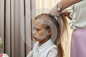 Close up photo of happy smiling schoolgirl with long hair and her mother who is combing her hair at home, they are dressed in