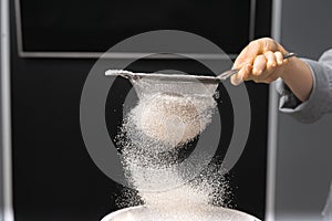 Close up photo of a human hand sieving flour and getting ready for baking.