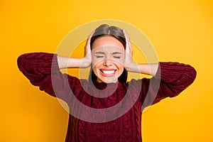 Close up photo of insane woman closing her ears eyes with palms wearing maroon pullover isolated over yellow background